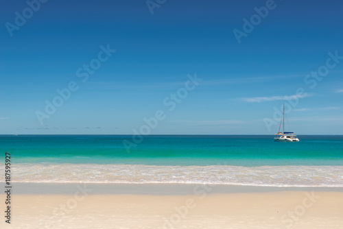 Tropical beach background with sailboat on horizon. 