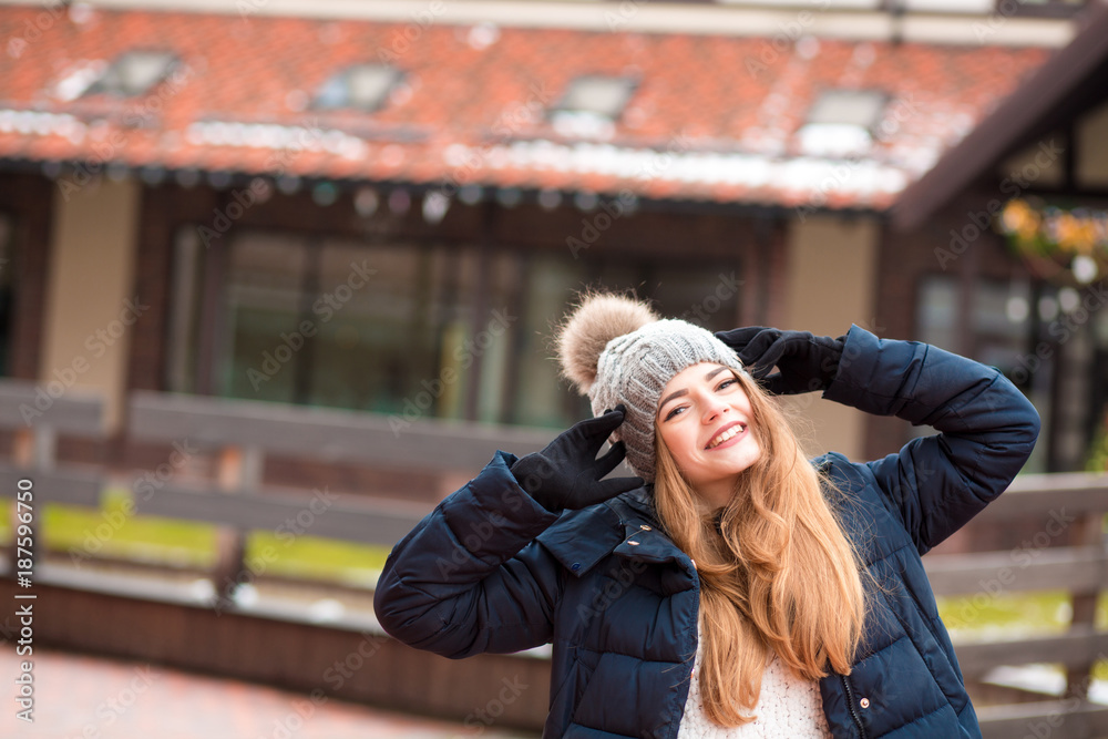 Fototapeta premium Happy red haired woman wearing black winter coat and knitted hat posing at the street in Kiev