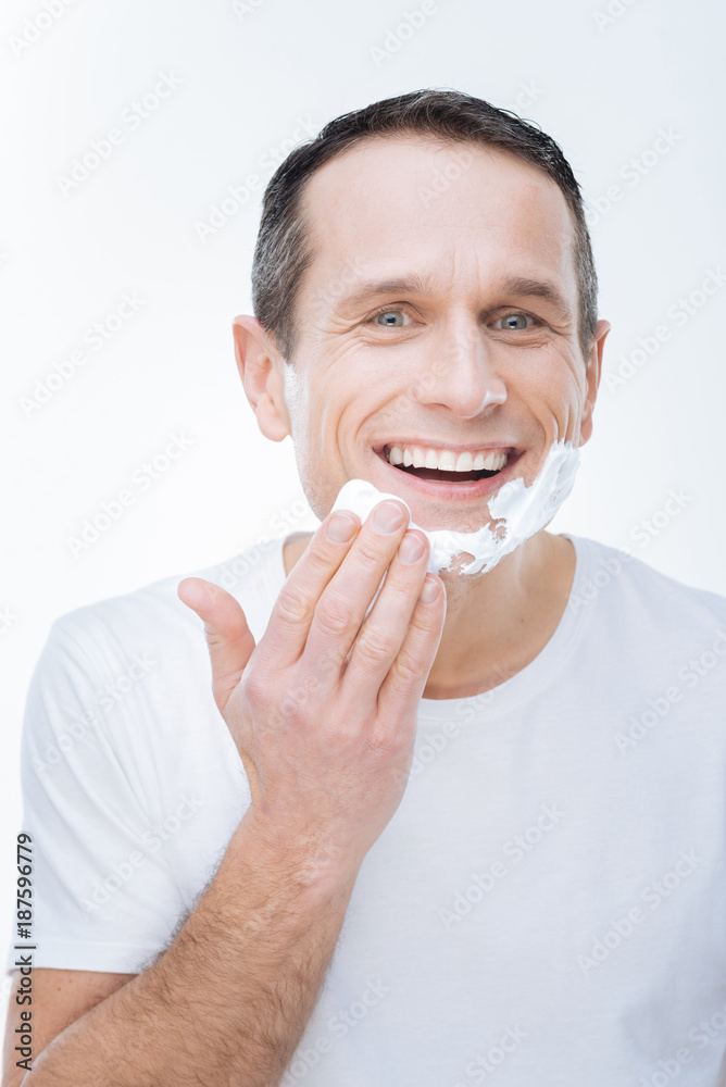 Morning shaving. Joyful handsome young man smiling and putting on shaving foam while being in a good mood Morning shaving. Joyful handsome young man smiling and putting on shaving foam while being in a good mood