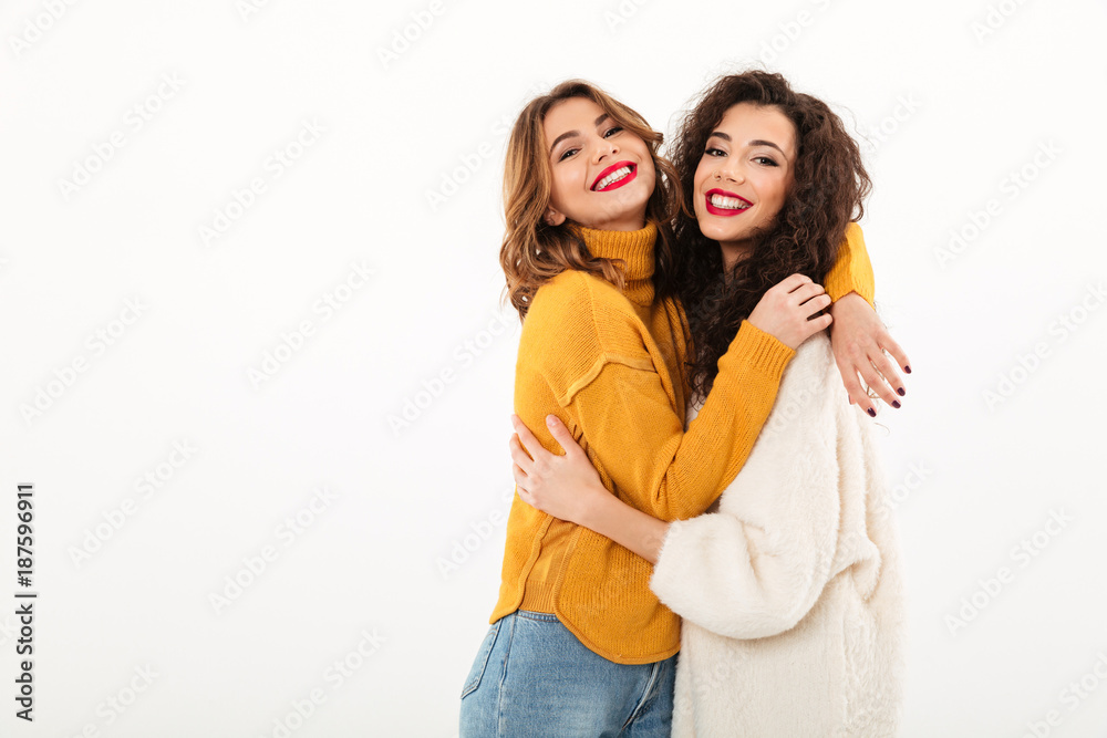 Two pleased girls in sweaters hugging to each other Two pleased girls in sweaters hugging to each other