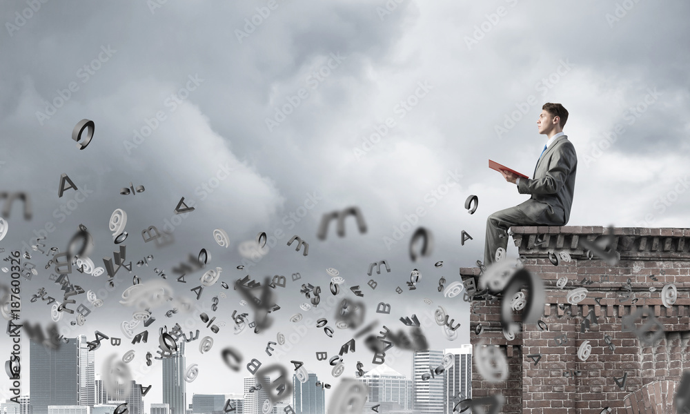 Man on roof edge reading book and symbols flying around Man on roof edge reading book and symbols flying around
