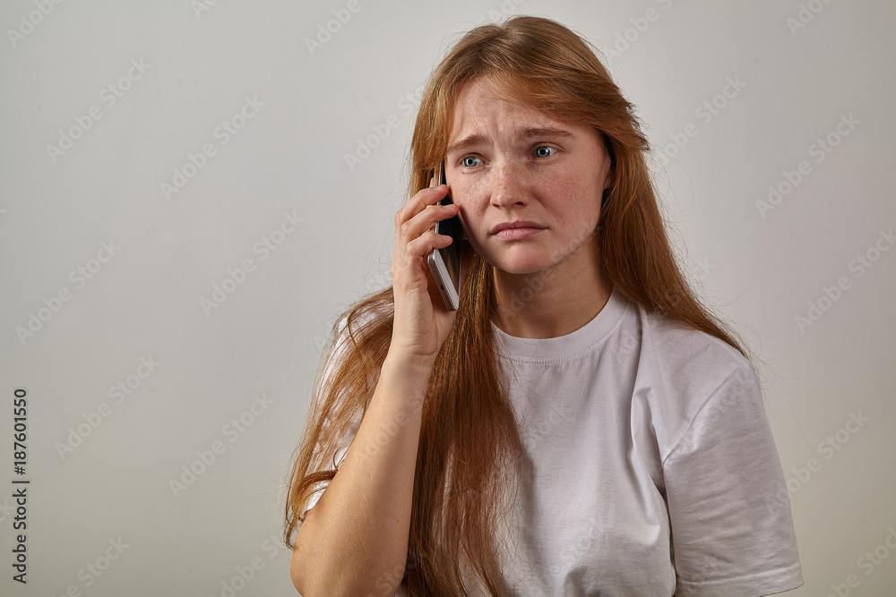 Studio indoor portrait of young red-headed girl with freckles holding her phone next to her ear and talking with sad expression on her face Studio indoor portrait of young red-headed girl with freckles holding her phone next to her ear and talking with sad expression on her face