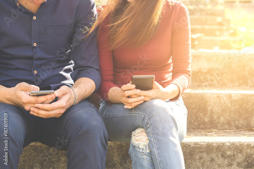 young couple socially ignoring each other because of their using their smartphones are sitting in a park, which conveys the concepts of social ignorance, phubbing and social network addiction