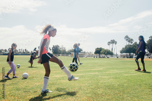 Schoolgirls practicing keepy uppy with soccer ball on school sports field photo