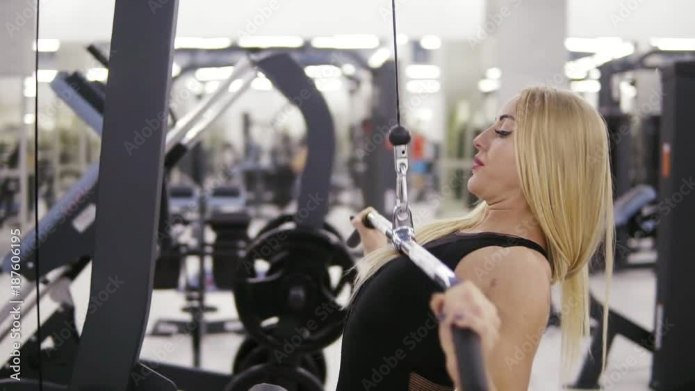 Attractive young blond caucasian woman with sporty body training hard on a lat pull-down mashine at the gym. Healthy lifestyle concept. Attractive young blond caucasian woman with sporty body training hard on a lat pull-down mashine at the gym. Healthy lifestyle concept.