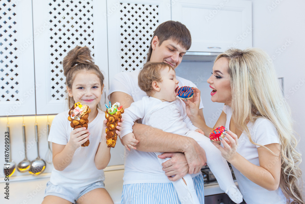 Funny family of four on the background of bright kitchen beautiful have fun fooling around eating donuts. The concept of family happiness. The full family. Funny family of four on the background of bright kitchen beautiful have fun fooling around eating donuts. The concept of family happiness. The full family.