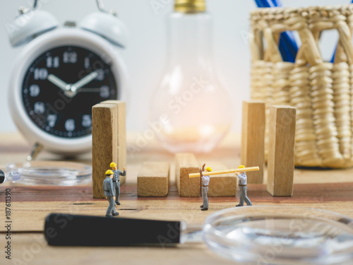 Miniature people engineer worker on wood table and white background . Around have a magnifying glass, clock and quare wood.