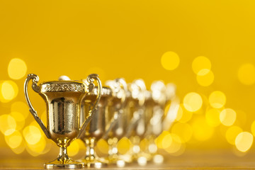 Gold award trophy against bright yellow background with blurred lights