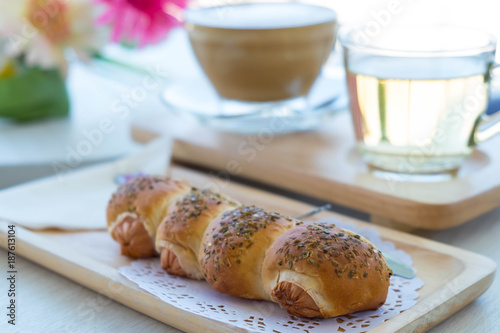Sausage bread on wooden plate with flower , cup of coffee and cup of tea in the background