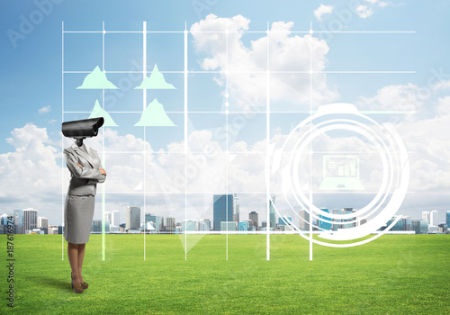 Camera headed woman standing on green grass against modern cityscape