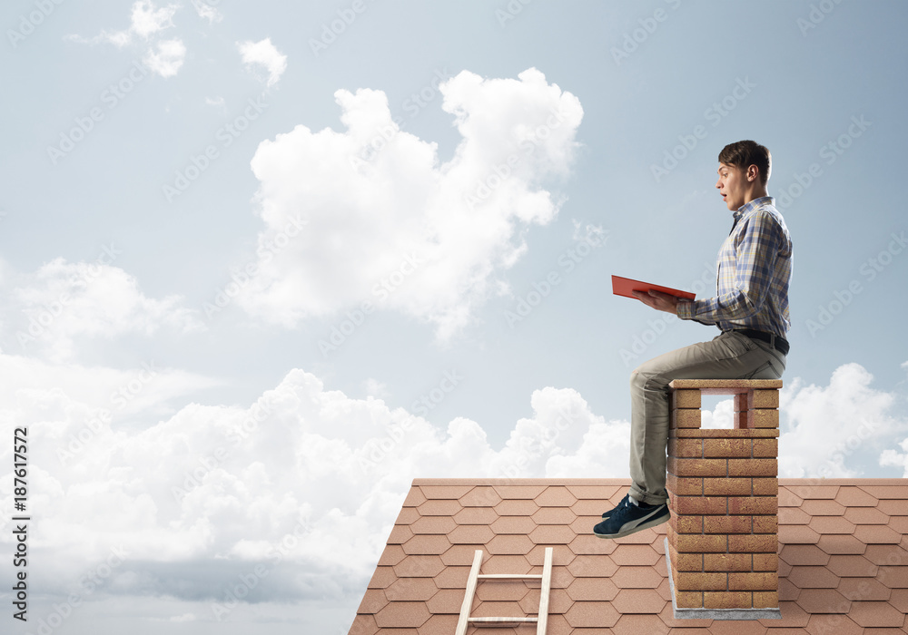 Handsome man on brick roof against cloud scape reading book Handsome man on brick roof against cloud scape reading book