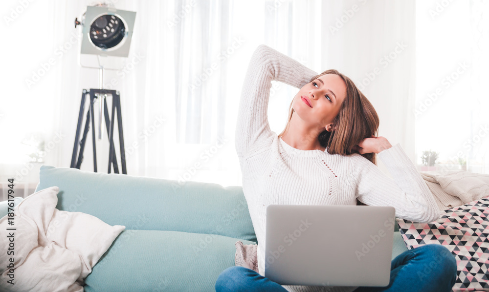 Woman at home sitting on sofa and stretching while working with laptop computer Woman at home sitting on sofa and stretching while working with laptop computer