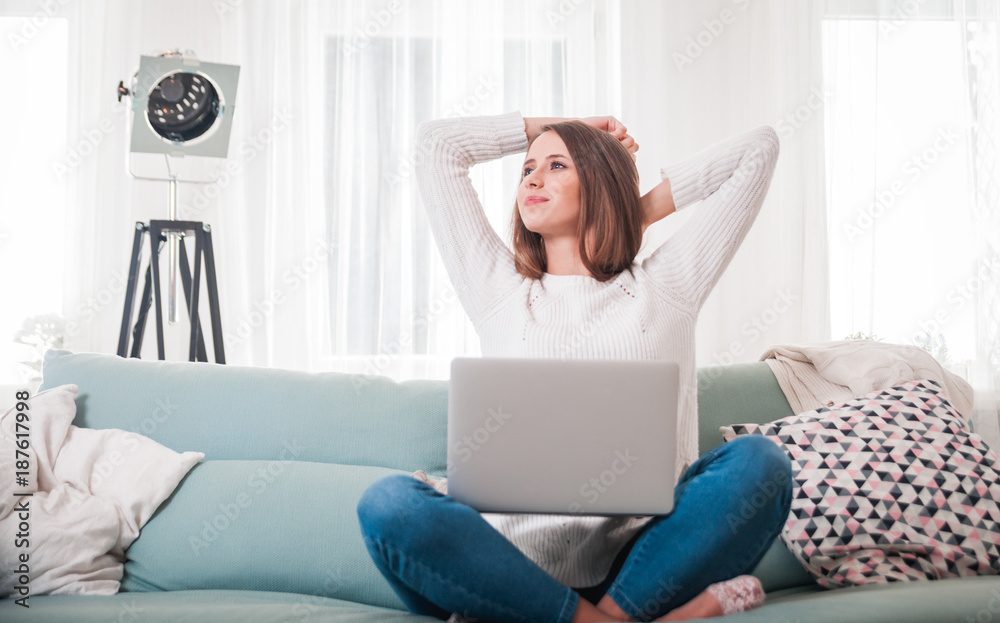 Woman at home sitting on sofa and stretching while working with laptop computer Woman at home sitting on sofa and stretching while working with laptop computer