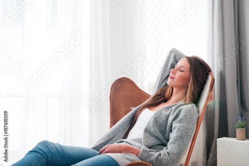 Woman at home sitting on modern chair near window relaxing in living room