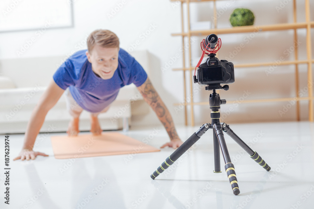 Doing pushups. Cheerful strong experienced trainer feeling glad while doing pushups in front of a modern camera