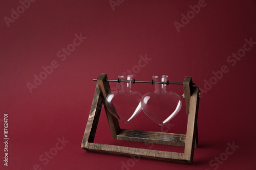 two empty heart shaped glass jars on wooden stand on red