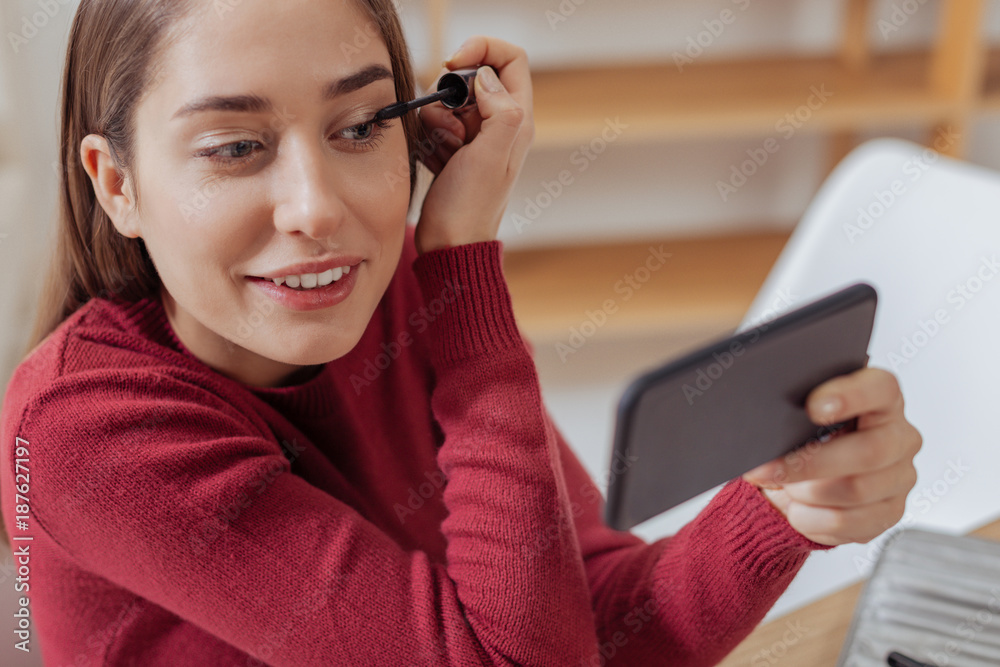 Significant detail. Calm concentrated young beauty blogger feeling satisfied while testing her new mascara and looking at the screen of her modern device Significant detail. Calm concentrated young beauty blogger feeling satisfied while testing her new mascara and looking at the screen of her modern device