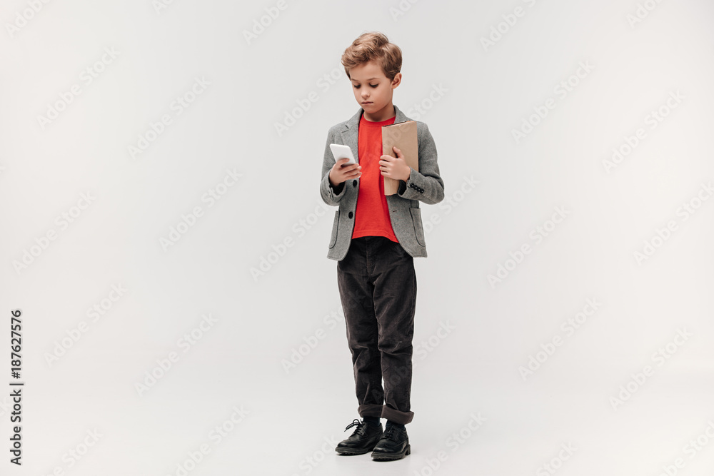stylish little schoolboy with smartphone and book isolated on grey stylish little schoolboy with smartphone and book isolated on grey