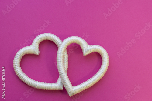 St. Valentine's Day or Anniversary concept with a wedding decoration- white satin hearts , pink background, top view