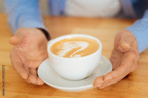 Its for me. Senior calm concentrated man sitting by the table spending time alone and holding hands near a cup of coffee.