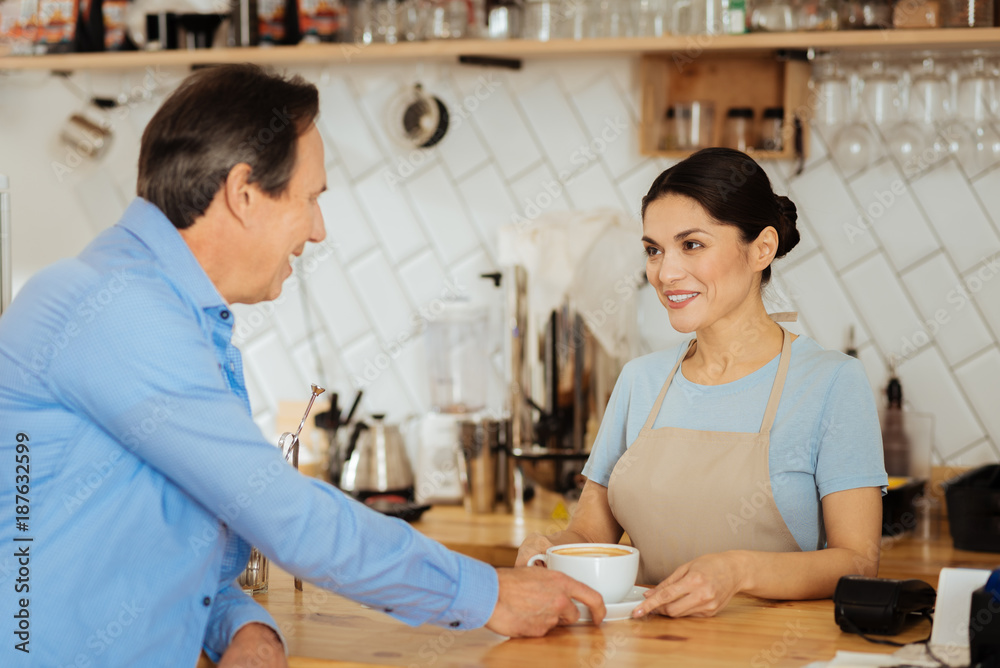 Just one offer. Pretty pleasant smiling waiter standing opposite a man communicating and touching to the cop of coffee. Just one offer. Pretty pleasant smiling waiter standing opposite a man communicating and touching to the cop of coffee.