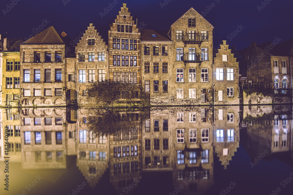 Ghent, Flanders, Belgium - January 2th, 2017. Night Gent Old town view with illuminated medieval merchant houses reflected on the water of canal by evening lights. City illumination.