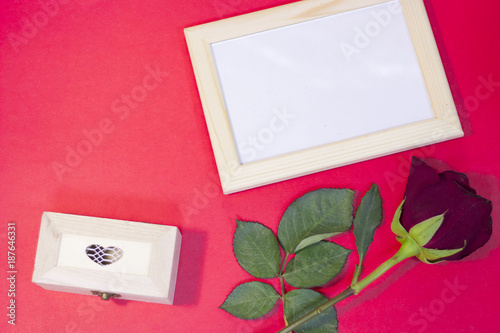 The concept of St.Valentine's Day with a beautiful red rose and wooden photo frame, red background, top view
