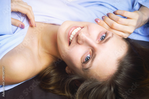 Closeup of young beautiful smiling woman in blue lying in bed. Natural beauty. Selective focus. Film style