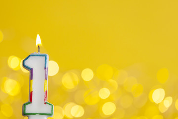 Number 1 birthday celebration candle against a bright lights and yellow background