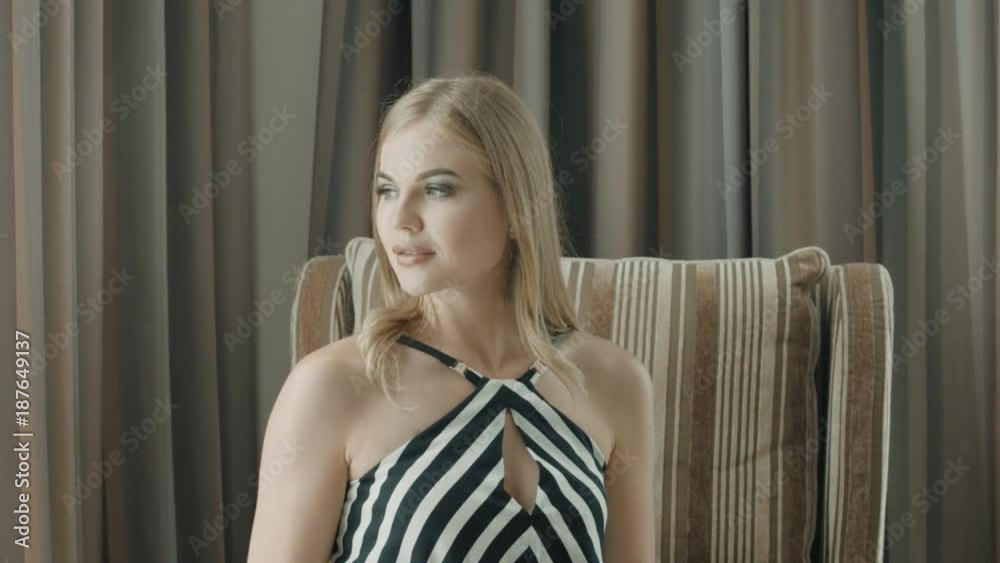 Cute blonde looks away sitting in an armchair in hotel room Cute blonde looks away sitting in an armchair in hotel room