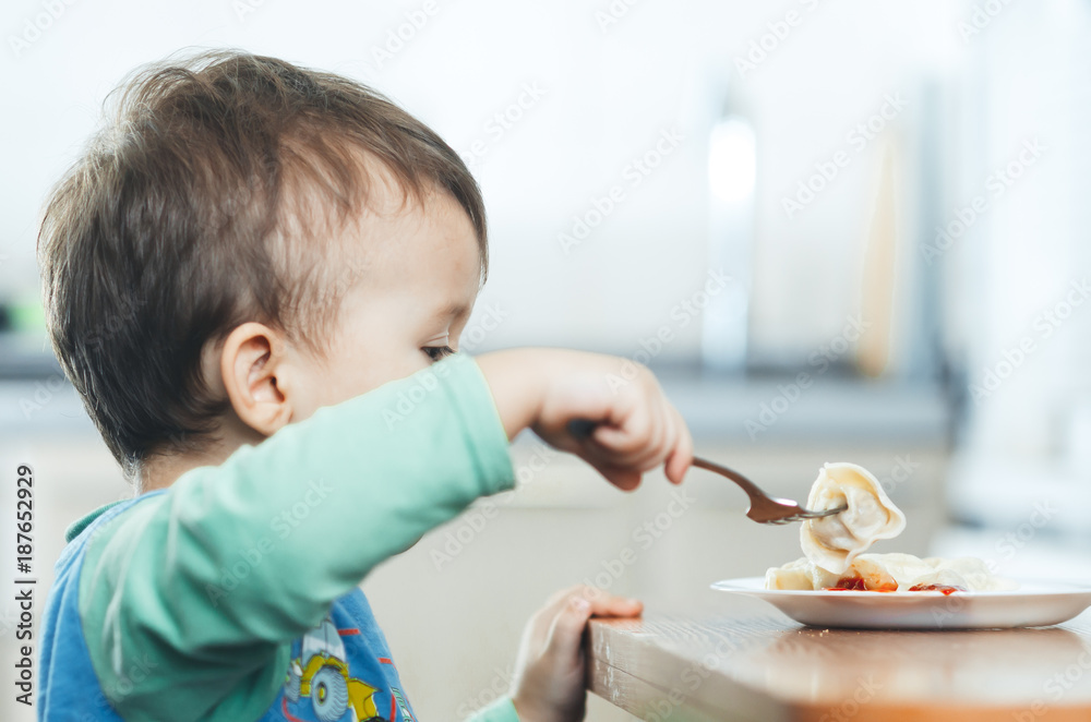 A hungry child is eating dumplings in the kitchen A hungry child is eating dumplings in the kitchen