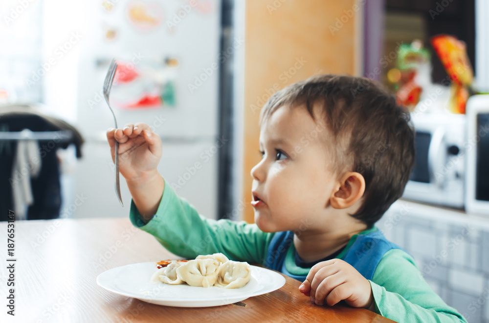 A hungry child is eating dumplings in the kitchen A hungry child is eating dumplings in the kitchen