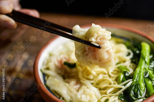 man eating shrimp wonton noodle soup with choy sum