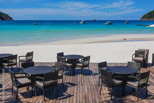 Wattled tables and chairs on wooden terrace in cafe on paradise beach with white sand and turquoise sea  Redang island  Malaysia