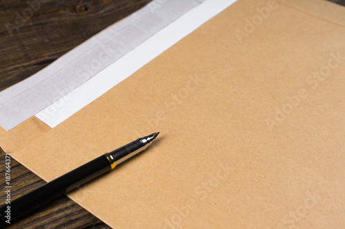 Envelope nested in it leaves lying on vintage wooden table. The fountain pen is opened and ready for writing of the text. A place for your inscriptions