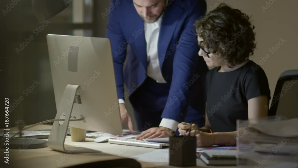 Businessman and female colleague working with documents at desk while staying in the office at night Businessman and female colleague working with documents at desk while staying in the office at night