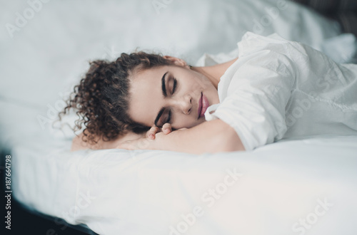 Beautiful woman sleeping in bed wearing white pajamas close up. Bedtime. 20s. Good morning.