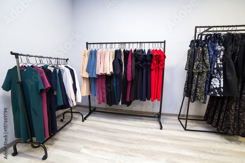 colorful women's dresses and other clothes on hangers in a retail shop. Fashion and shopping concept