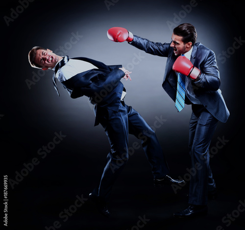 Two young businessman boxing againts dark background.