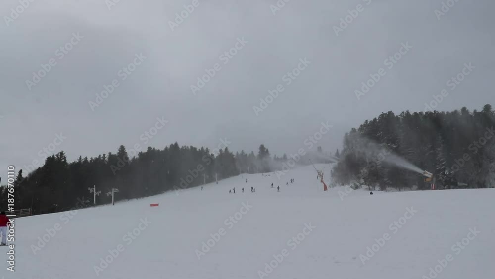 People do skiing on the mountainside. Skiers go down the snow slope. Snow maker machines make snow. People do skiing on the mountainside. Skiers go down the snow slope. Snow maker machines make snow.