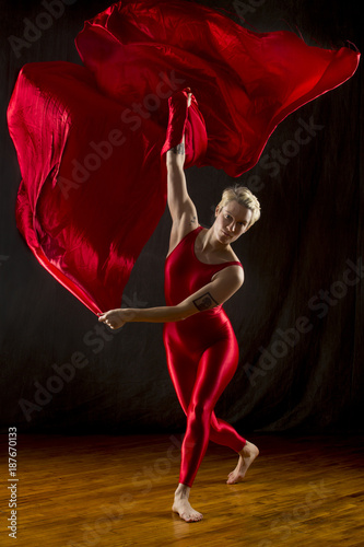 Fototapeta Naklejka Na Ścianę i Meble -  Young woman in red unitard swirling red fabric in studio.
