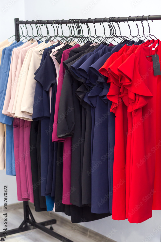 colorful women's dresses and other clothes on hangers in a retail shop. Fashion and shopping concept