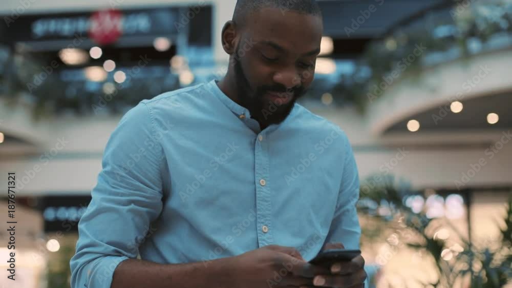 Attractive smiling african american young man using phone standing in shopping center feel happy christmas internet face technology black telephone portrait cute close up mobile holding slow motion Attractive smiling african american young man using phone standing in shopping center feel happy christmas internet face technology black telephone portrait cute close up mobile holding slow motion