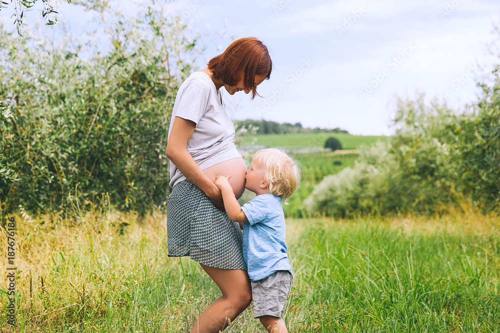 Φωτογραφία Child boy kissing belly of pregnant her mother on nature background