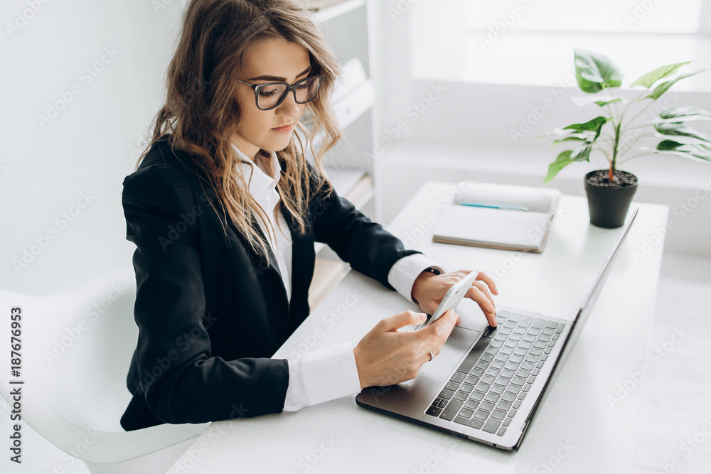 Young attractive business woman working in her office with a laptop and looks into the phone Young attractive business woman working in her office with a laptop and looks into the phone