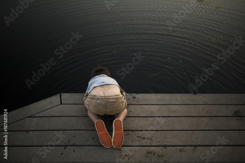 High angle view of boy looking in lake while kneeling on pier at park