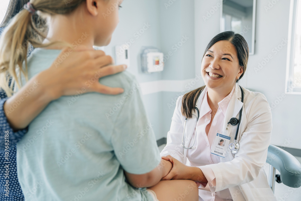 Cheerful pediatrician holding girl's hand sitting by mother in medical examination room Cheerful pediatrician holding girl's hand sitting by mother in medical examination room