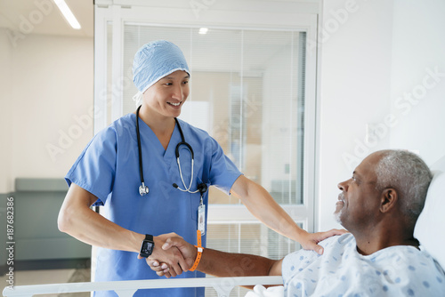 Confident surgeon shaking hands with senior patient in hospital ward photo