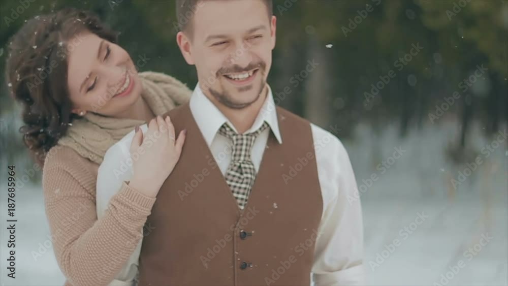loving couple walking in winter christmas park and smiling. The snowfall. Rustic Style. Lovely Girl in Long Wedding White Dress Smiling, Green Pine Forest on Background. Brown Style Wedding. Slow loving couple walking in winter christmas park and smiling. The snowfall. Rustic Style. Lovely Girl in Long Wedding White Dress Smiling, Green Pine Forest on Background. Brown Style Wedding. Slow