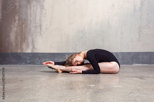 Young adult ballet dancer performing exercise while sitting on floor